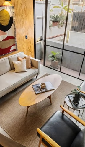 Overhead view of a living room with a bold woven tapestry, cream sofa, leather chairs, and steel-frame windows to a patio