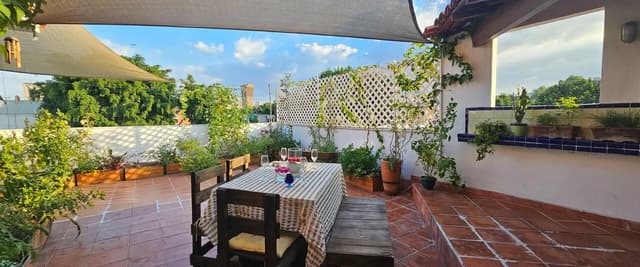 Rooftop terrace with dining table, chairs, and kitchen area overlooking colonial church with red dome and surrounding buildings.